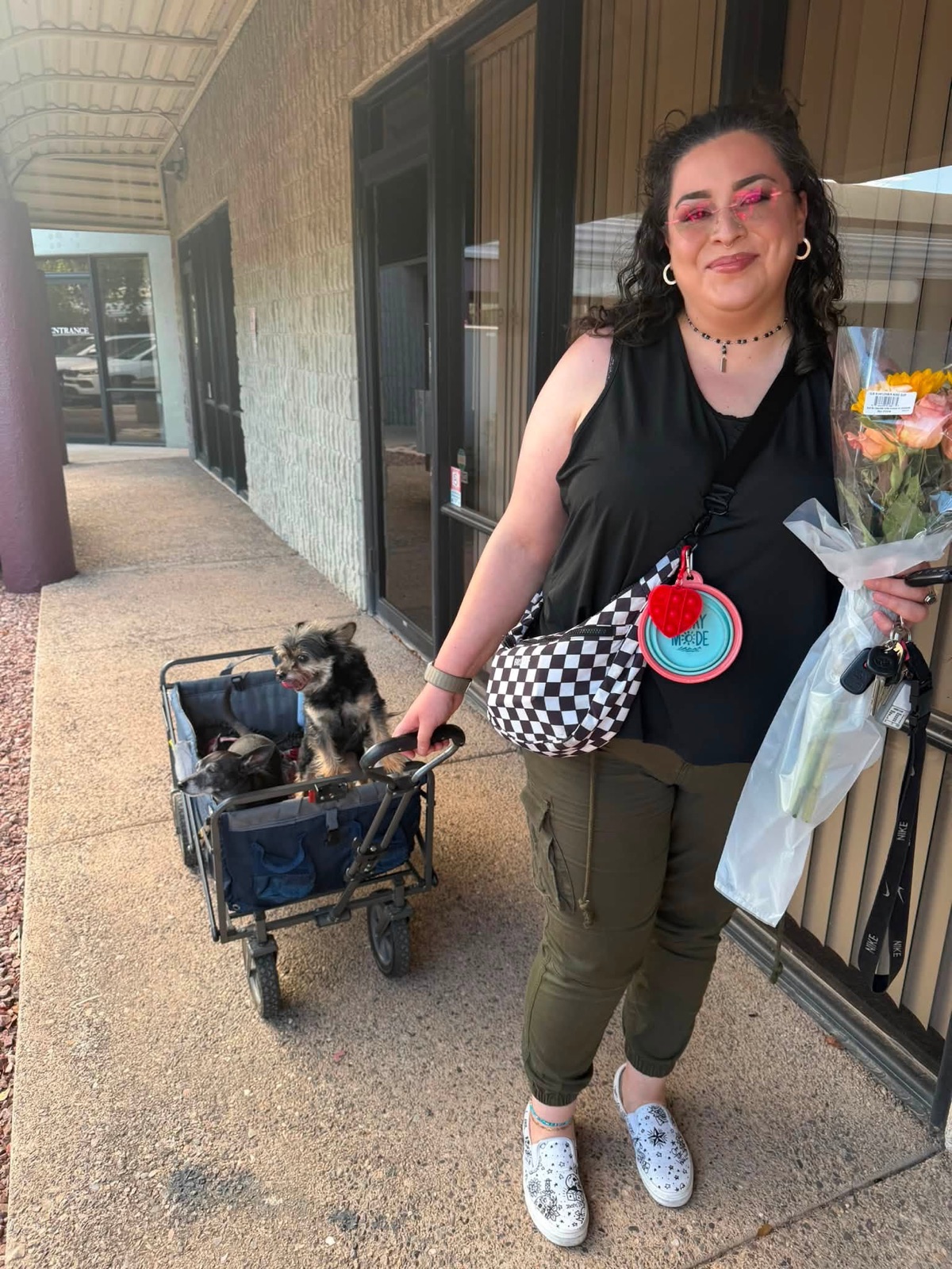 A person holding flowers beside two small dogs riding in a wagon outside the studio.