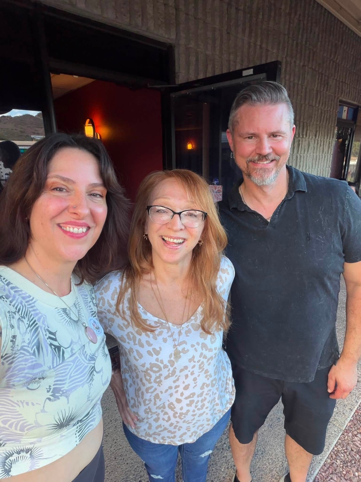 Three smiling people standing together at the open studio door.
