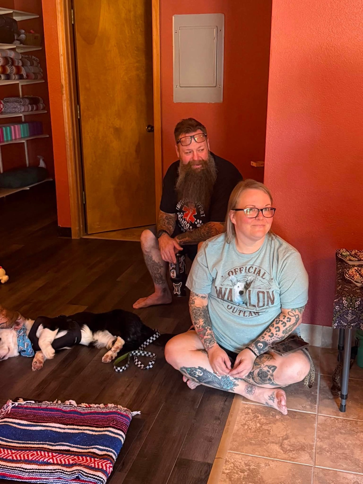 Two people sitting comfortably inside the studio with two dogs resting nearby.