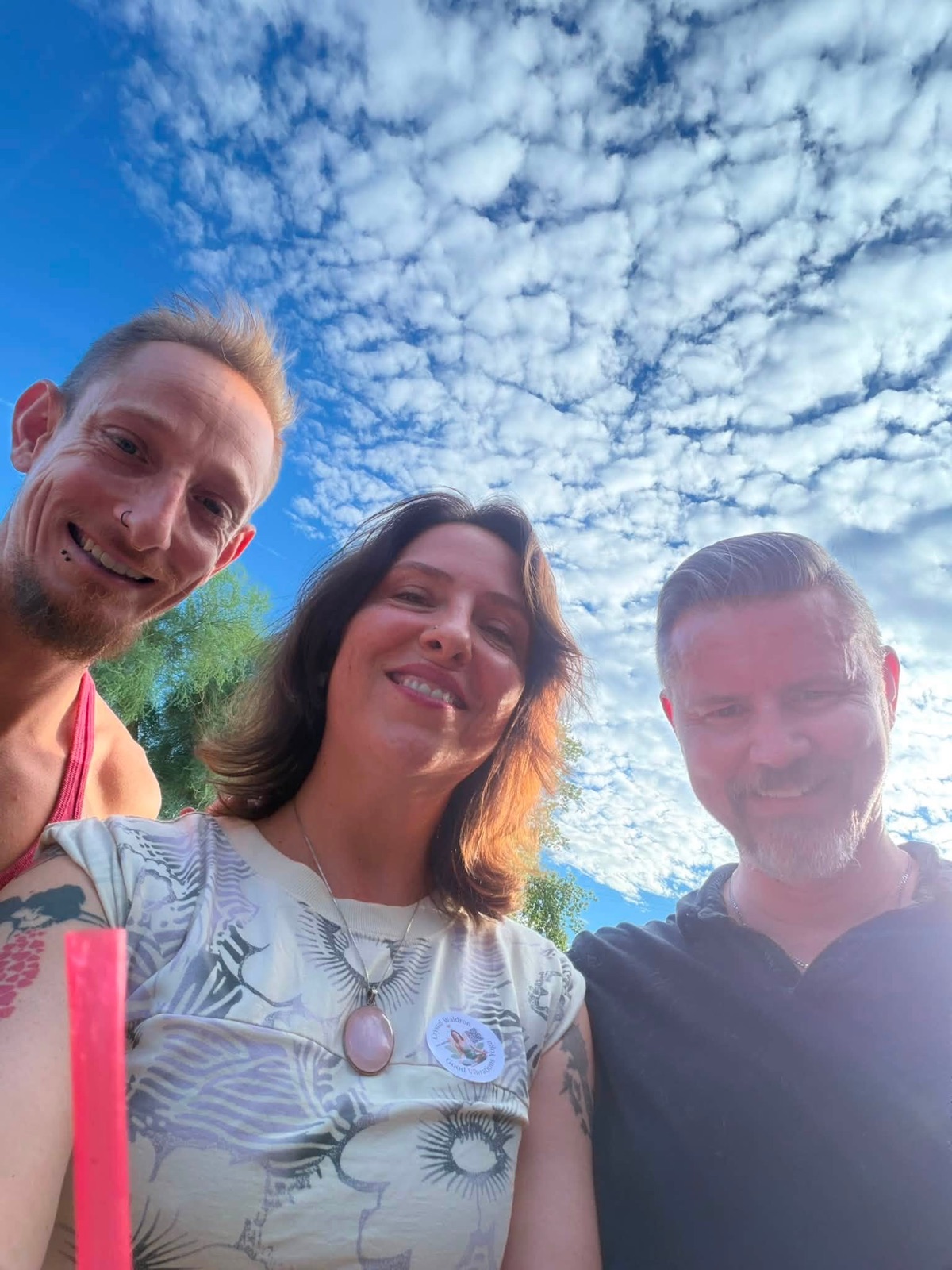 Three smiling people taking a photo together outside the studio entrance.