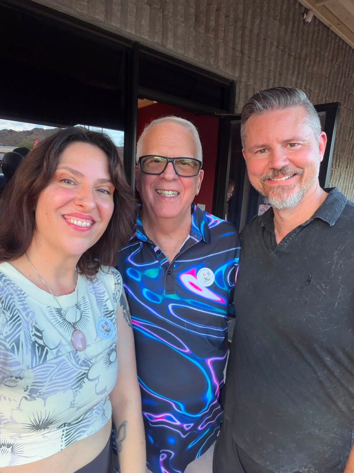 Three people taking a sunny outdoor selfie beneath a cloud-filled sky.